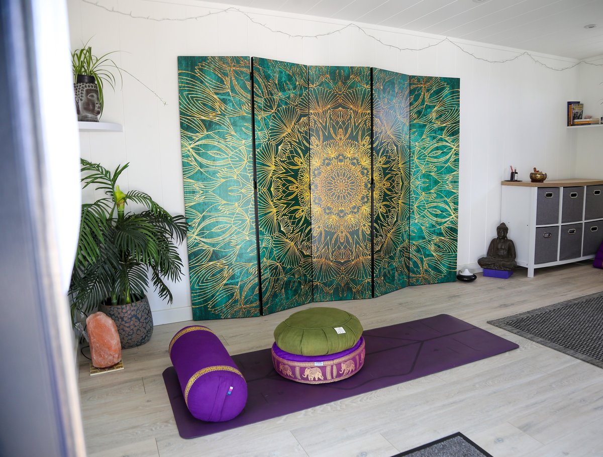 The studio's gold and green mandala room divider screen, with meditation cushions and bolsters set out in front